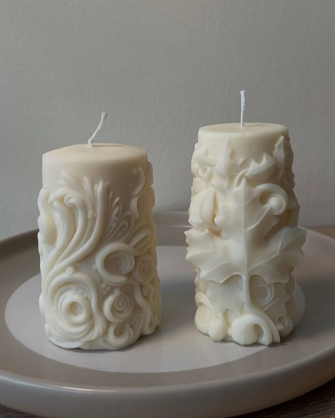 Two carved pillar candles with botanical relief on a plate