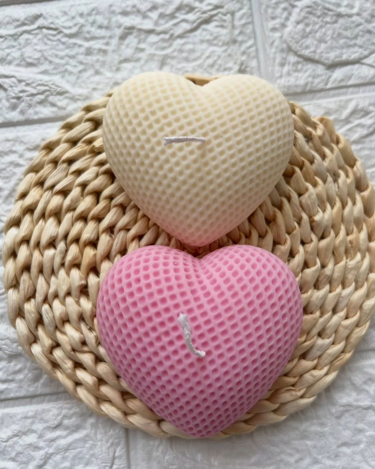 Two heart candles, cream and pink, on a straw mat